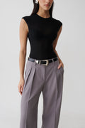 A model wearing a black sleeveless textured top and high-waisted gray pleated trousers with a black belt featuring a silver buckle, shot against a light gray studio background.