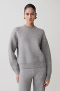 Woman wearing a gray sweater and pants on a plain background.