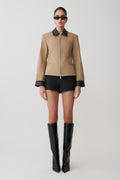 Person wearing a beige jacket with black accents, black shorts, and black knee-high boots on a white background.