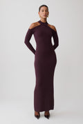 A woman modeling a long-sleeve, high-neck, bodycon maxi dress in a deep plum purple color, styled with pointed-toe heels against a light gray studio background.